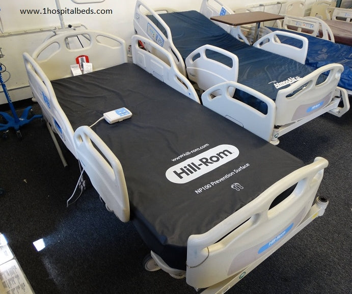 Hospital bed with foam mattress from Hill Rom Care Assist series, featuring adjustable side rails and control panel.